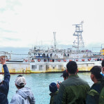 Men on shore wave at a fishing vessel
