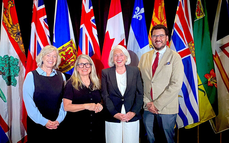 Canadian officials standing in front of the country's national and provincial flags