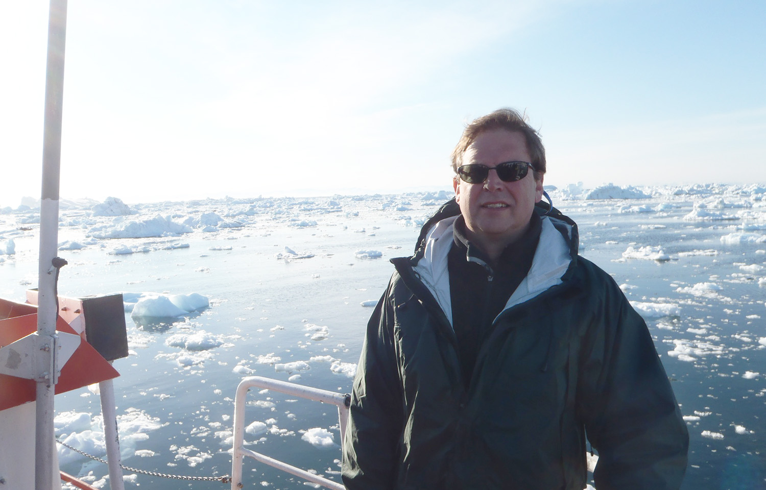 A photo of Sebastian Belle on board a boat, with a calm sea covered in ice in the background