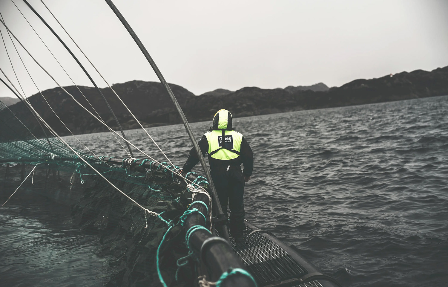 A Grieg Seafood farmer tending to a net pen on the open ocean