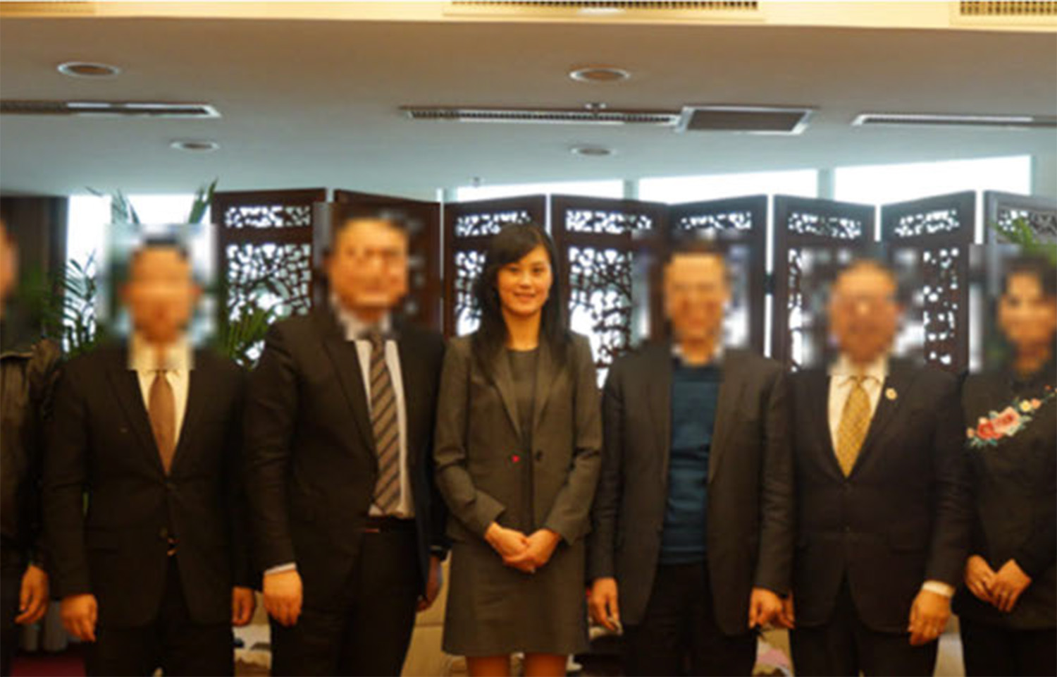 A photo of Linda Sun with several Chinese officials, with the officials' faces blurred.