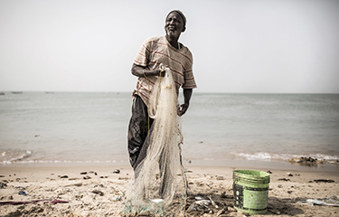 A Senegalese fisherman holding a net stands on the shoreline of Senegal.