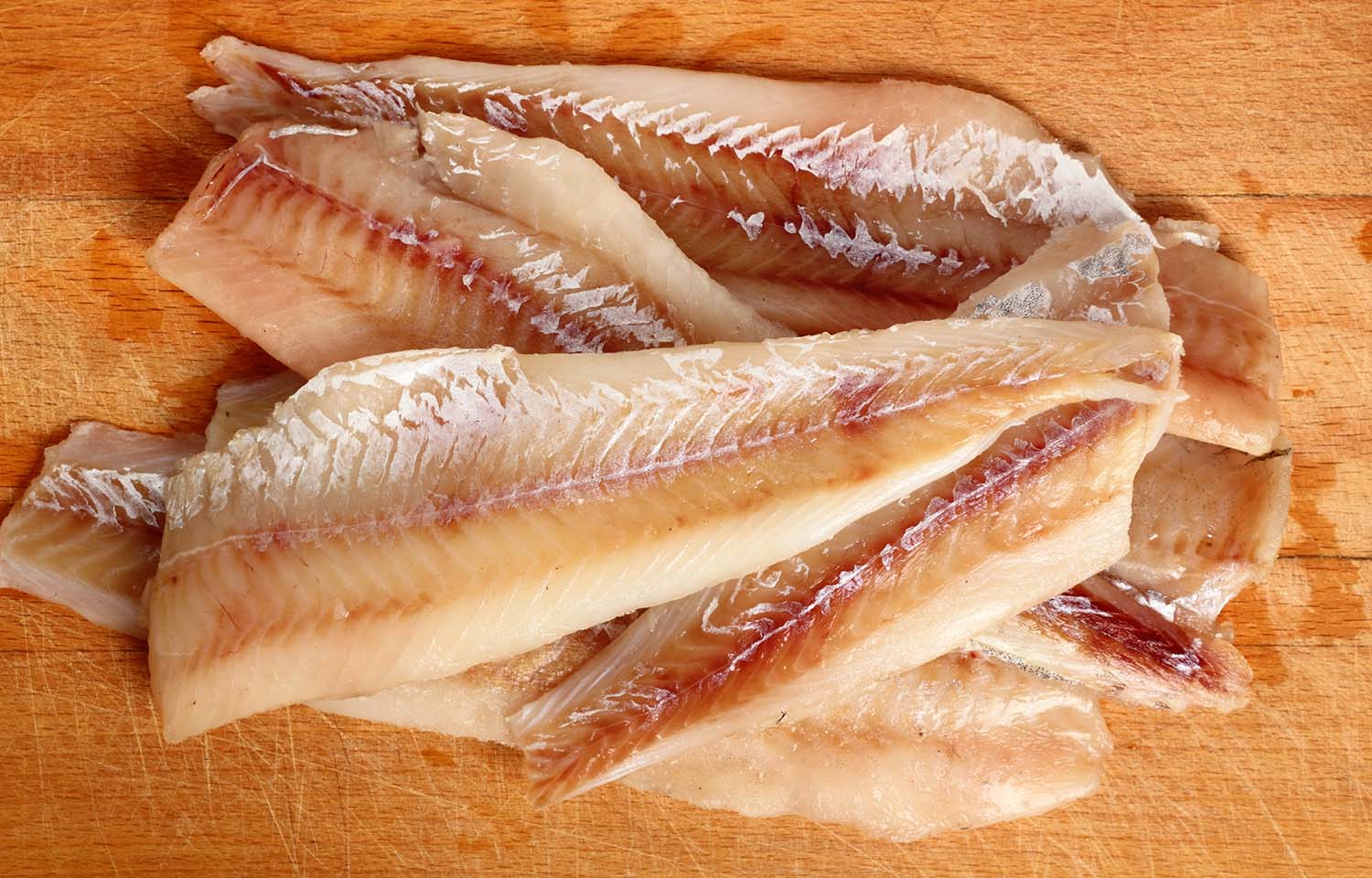 A pile of pollock fillets on a wooden cutting board.