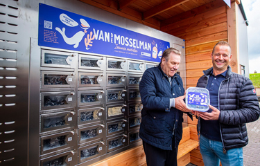 Two men show the packaged mussels you can purchase from a new mussel vending machine.